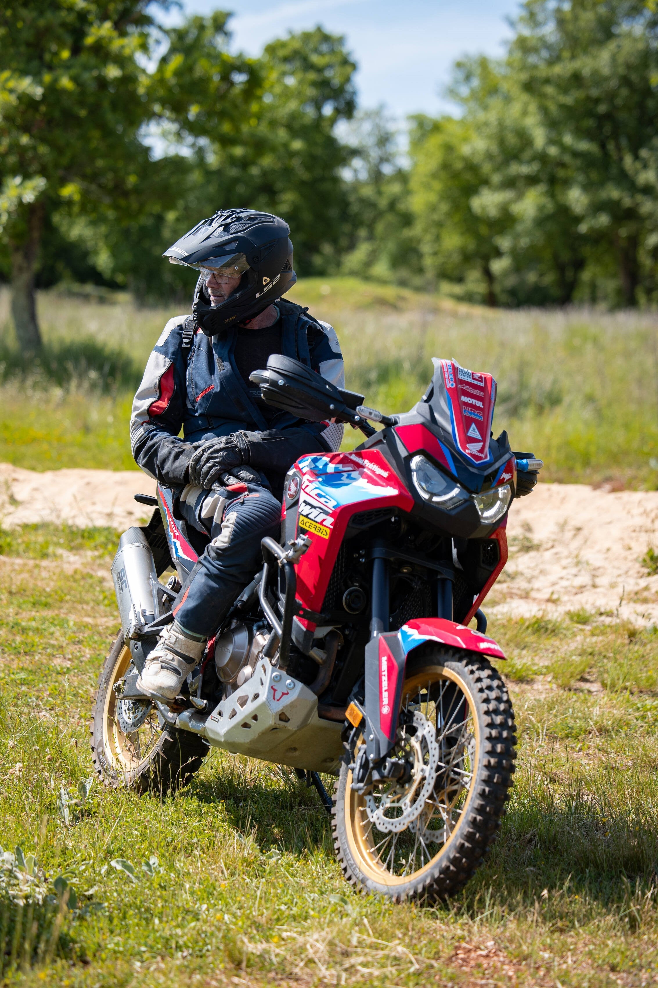 Honda CRF1100L Africa Twin con allestimento fuoristrada, pilota fermo in sella su prato