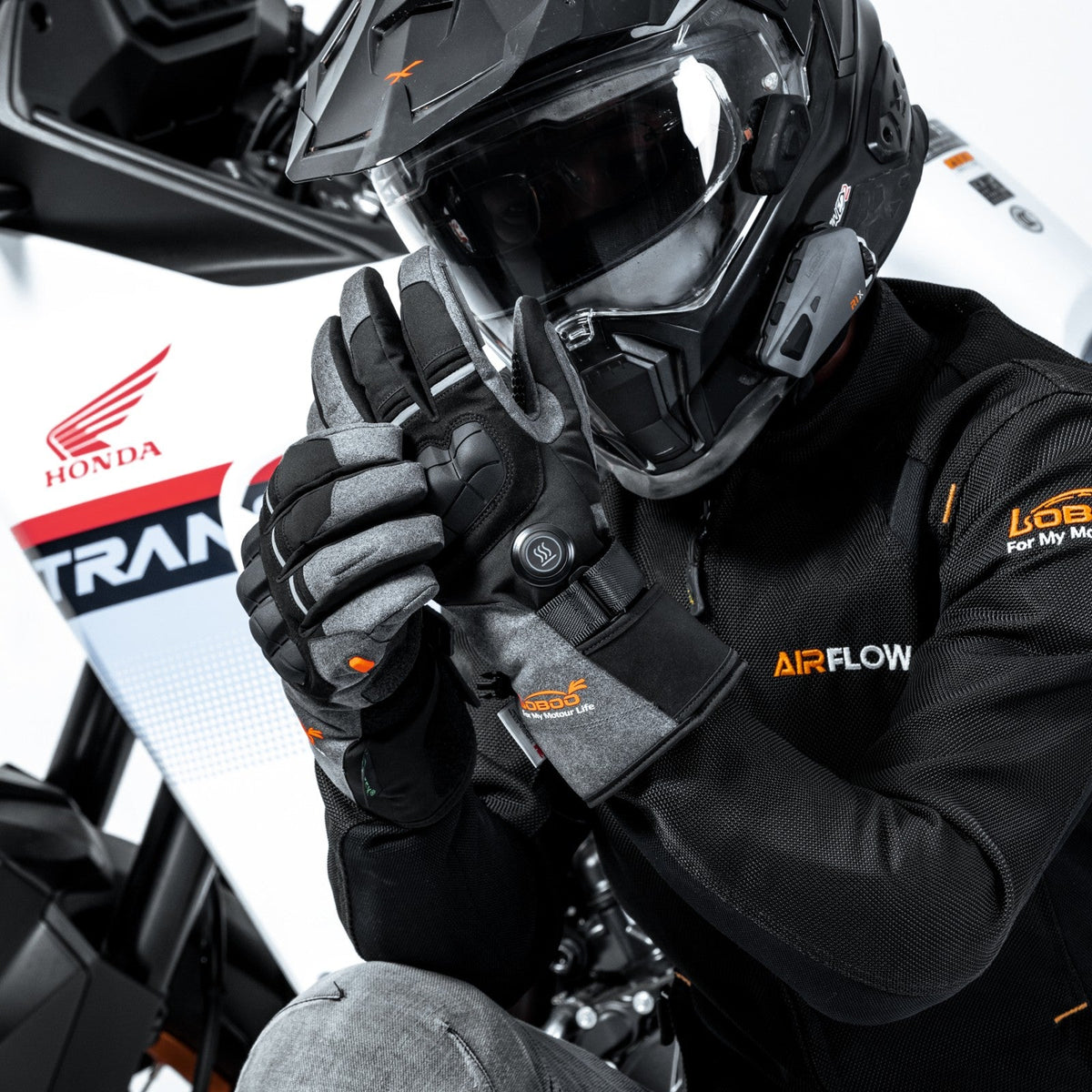 Motociclista con casco da adventure che sistema i guanti riscaldati accanto alla moto